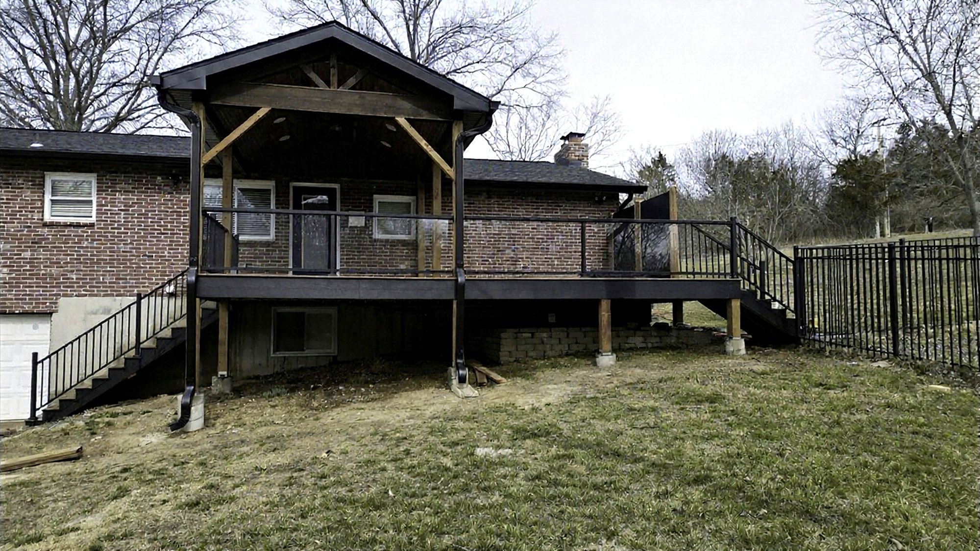 Covered deck with a cedar gable roof and black railings on a brick ranch house